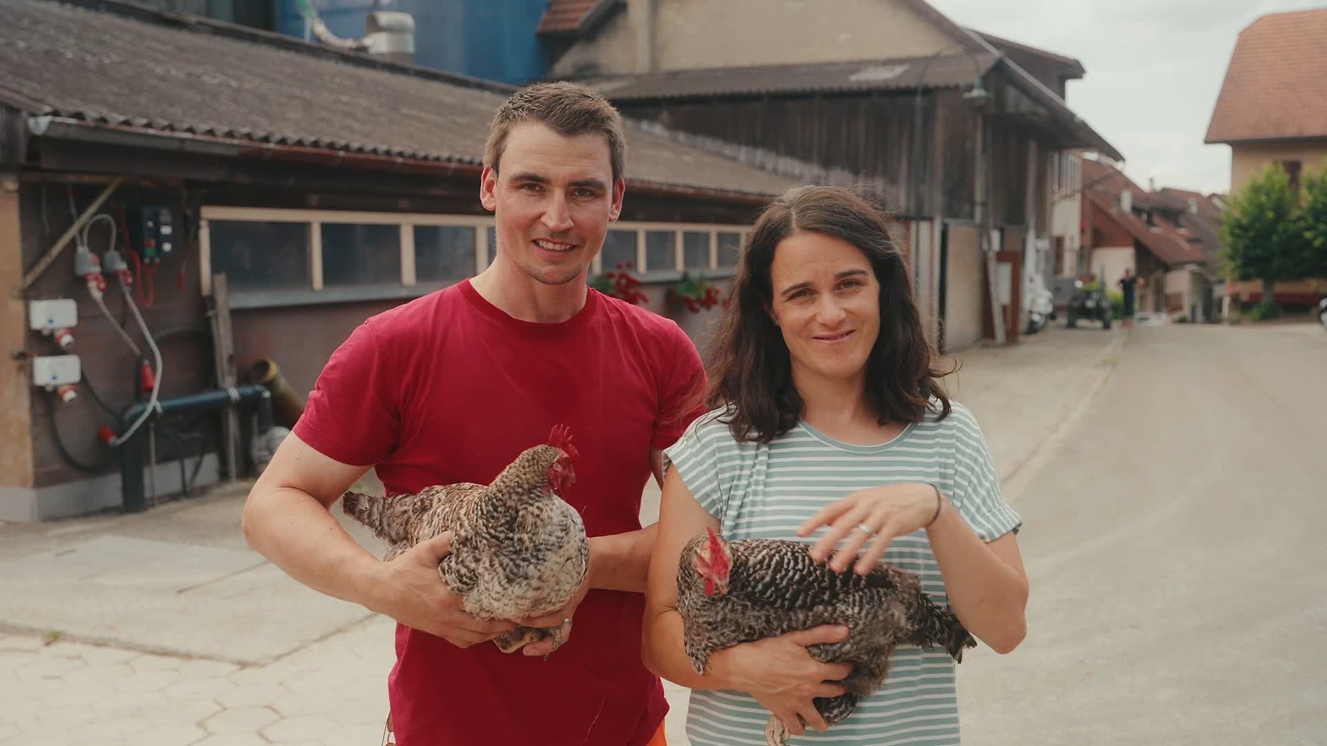 Rahel und Christoph Stocker mit Hühnern auf den Armen schauen in die Kamera