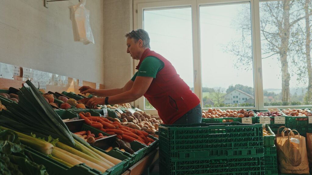 Jemand füllt Gemüse im Hofladen auf.