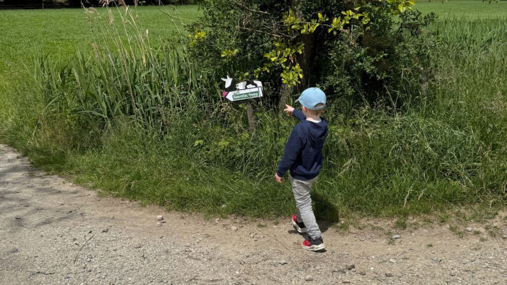 Ein Junge zeigt mit dem Finger auf ein Schild am Wegrand.